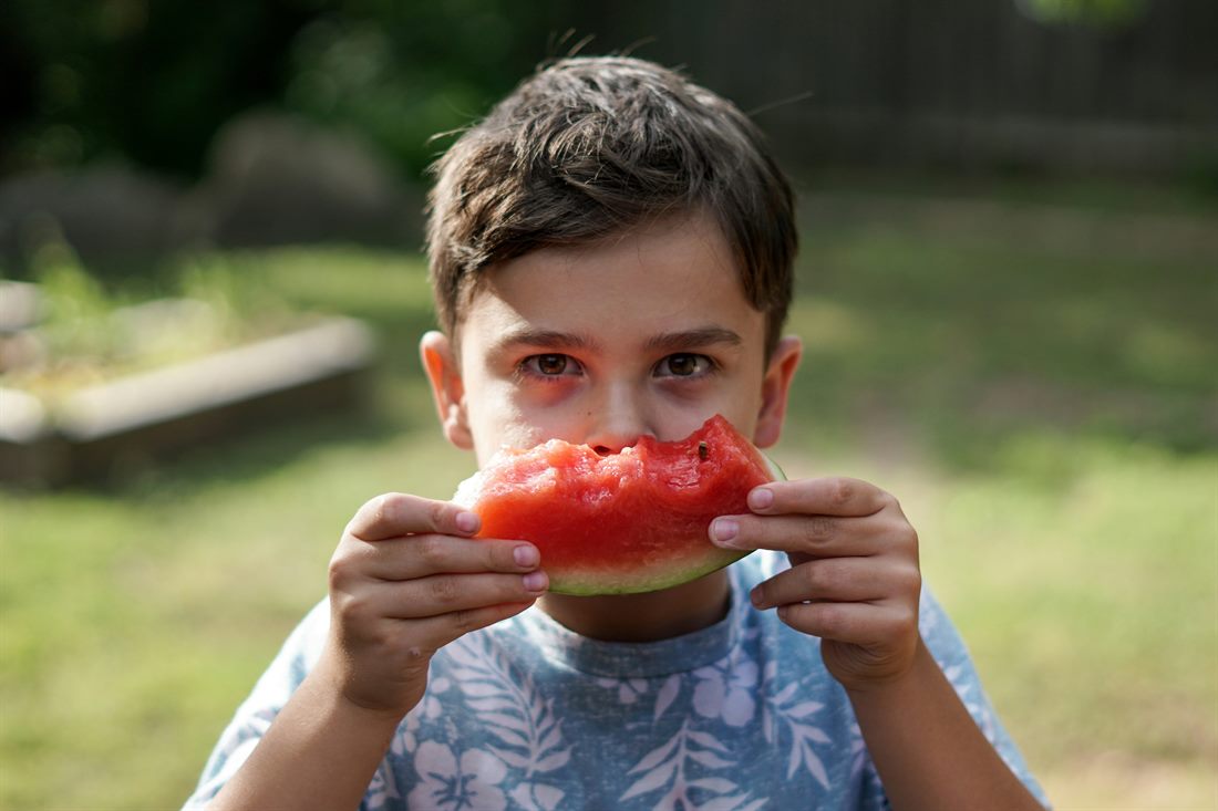 Niño comiendo sandía en un jardín